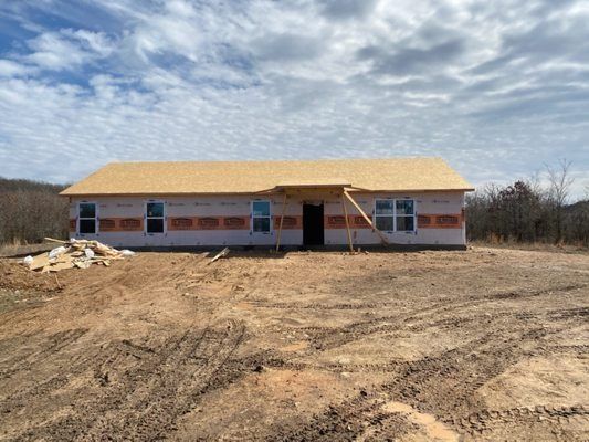 Partially built house with orange roof in a bare dirt lot under a cloudy sky