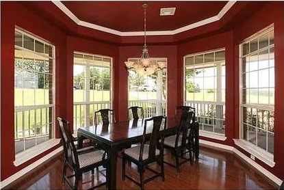 Elegant dining room with red walls, large windows, dark wood table, and chandelier
