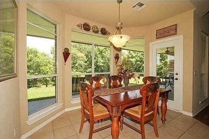 Bright dining room with wooden table, chairs, and large bay windows overlooking a green yard