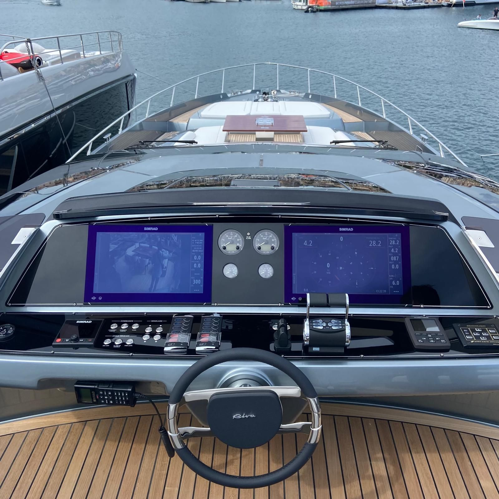 Postazione di comando di uno yacht di lusso con doppio schermo, comandi e volante che si affacciano sull'acqua.