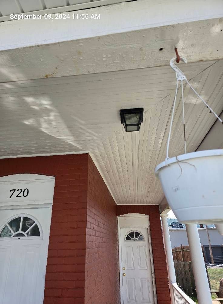 Porch of a red brick house with two white front doors, a hanging planter, and an overhead light fixture.
