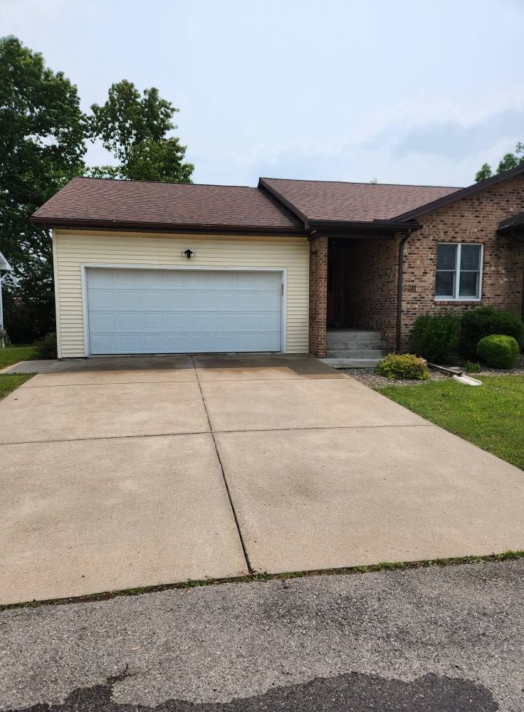 A brick and light yellow siding house with a one-car garage and a concrete driveway on a sunny day.