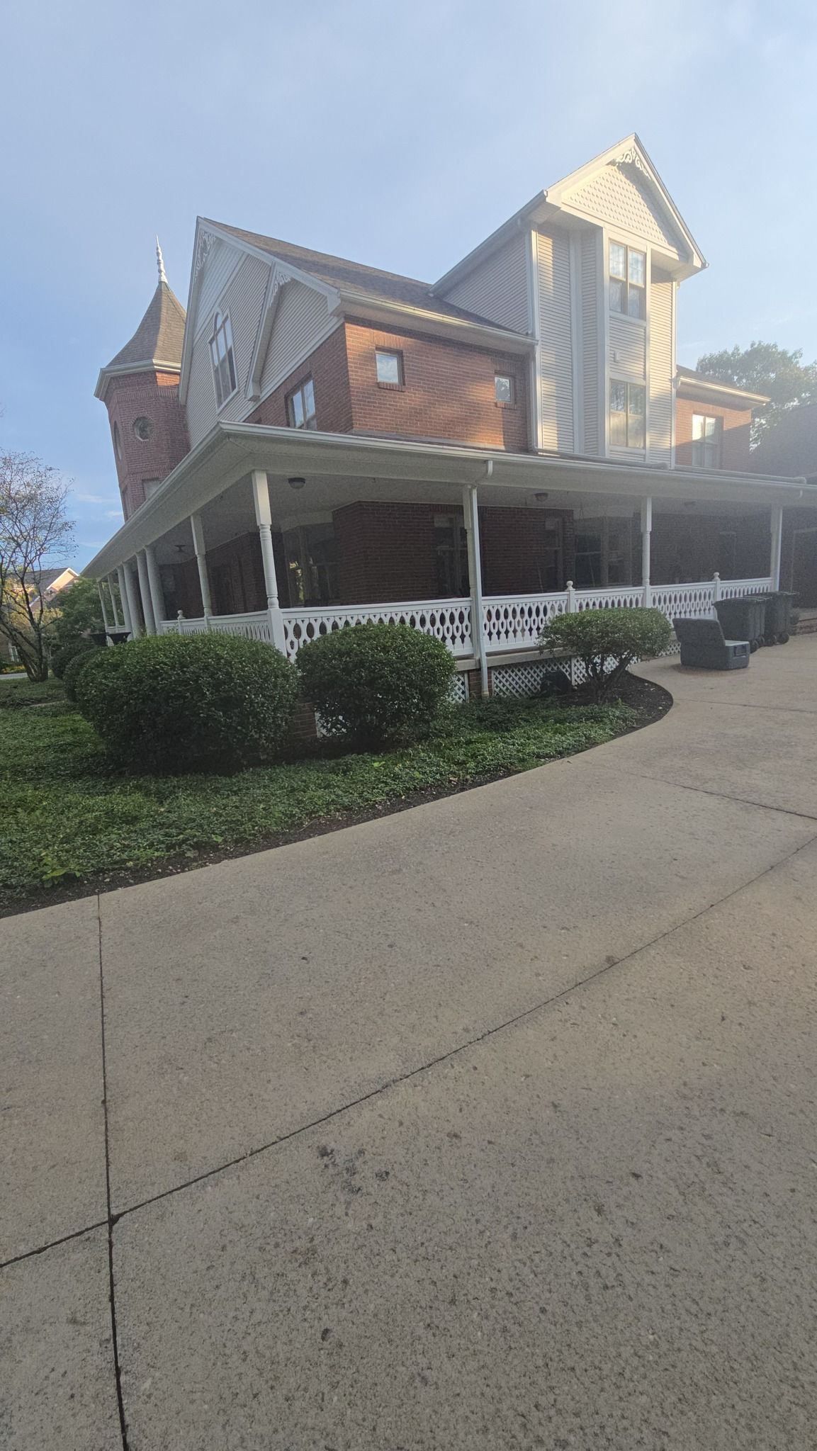 A two-story brick and siding house with a prominent front porch, a small turret, and a sidewalk leading to the entrance.