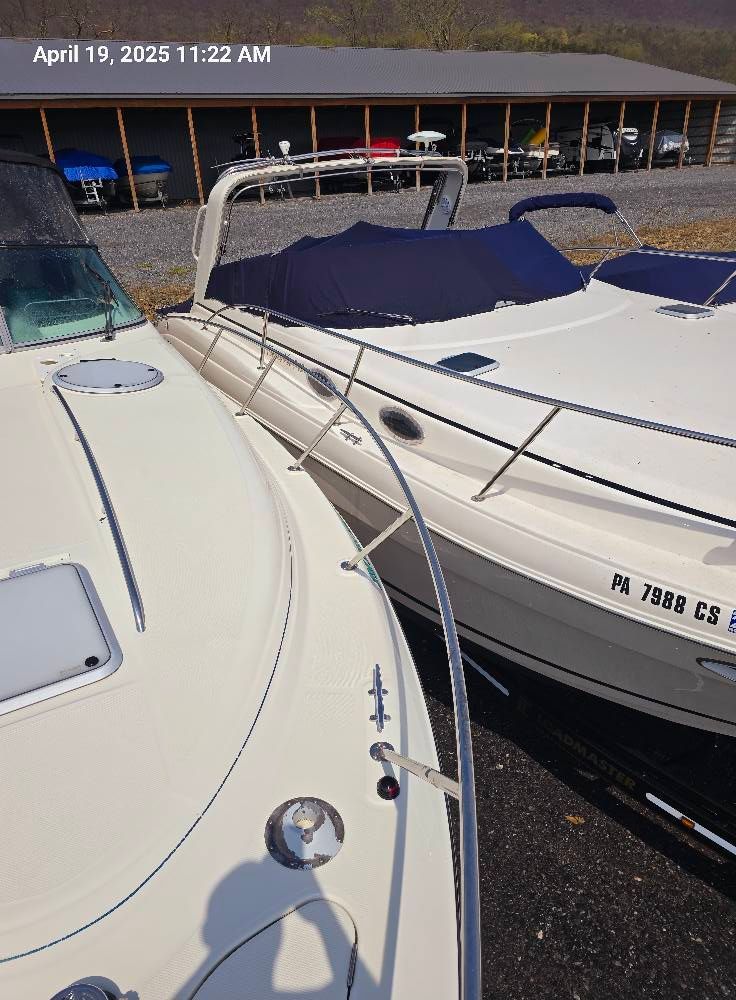 Two white motorboats are docked side-by-side in a storage yard with a building in the background.
