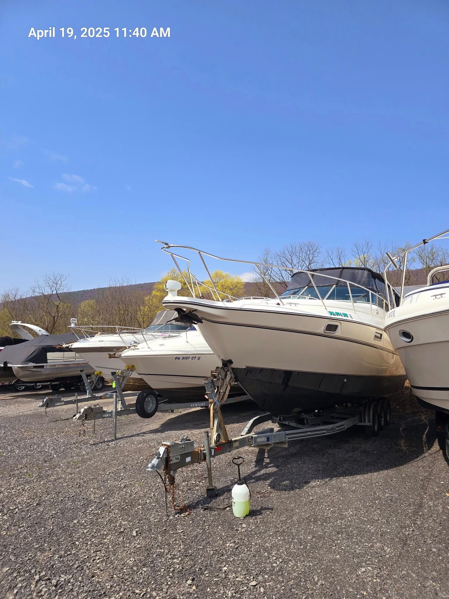Several motorboats on trailers in a gravel boat storage yard under a clear blue sky.