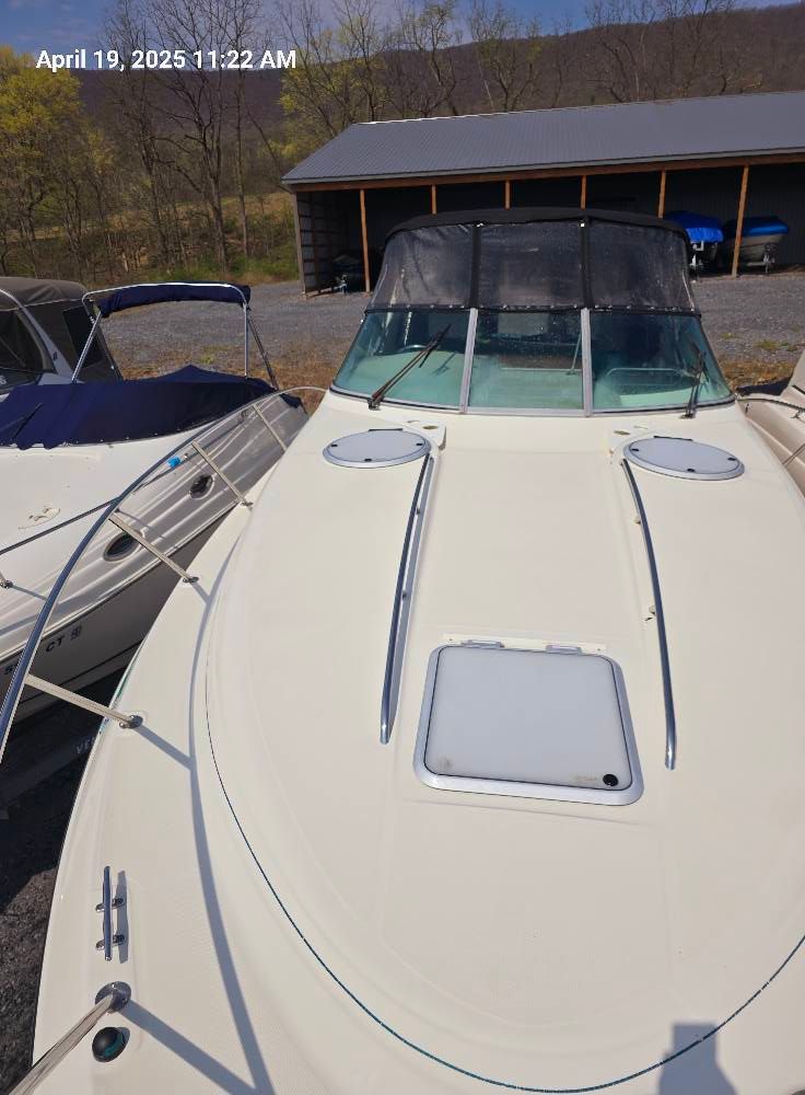A white motorboat with a black canopy is parked on a gravel lot next to another boat.