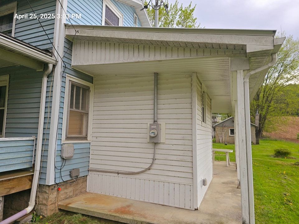 Side view of a white single-story home addition with an electric meter and small concrete porch next to a blue house.
