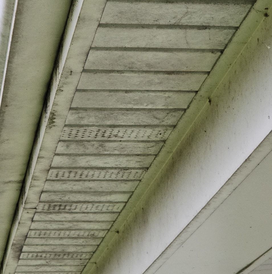 A close-up view of dirty, white vinyl soffit panels under a roof eave showing visible grime and mildew.