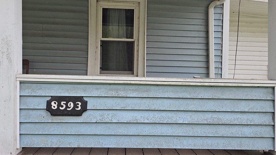 The number 8593 displayed on a black sign mounted to the blue horizontal siding of a porch.