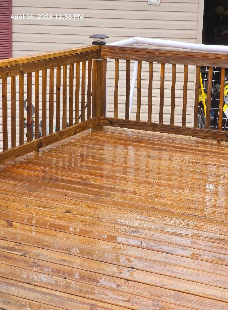 A wet, freshly stained wooden deck with vertical railings in front of a house with beige siding.