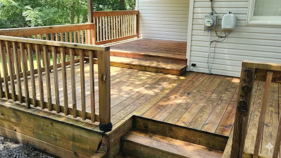 A wooden deck attached to a house features steps leading to a raised landing, surrounded by a wooden railing.