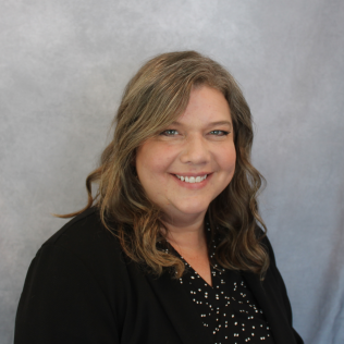 A woman wearing a black jacket and polka dot shirt smiles for the camera