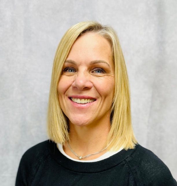 A woman with blonde hair is wearing a black sweater and smiling.