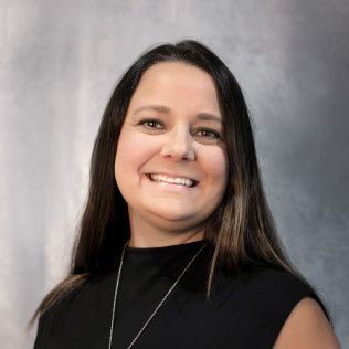 A woman wearing a black shirt and a necklace is smiling for the camera.