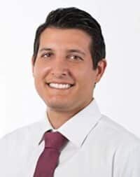 A man in a suit and blue shirt is smiling for the camera.