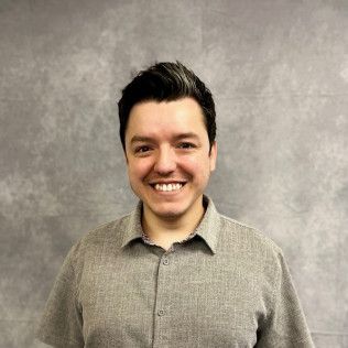 A man in a grey shirt is smiling for the camera.