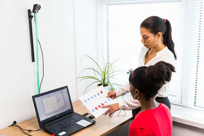 Two women are sitting at a desk in front of a laptop computer.
