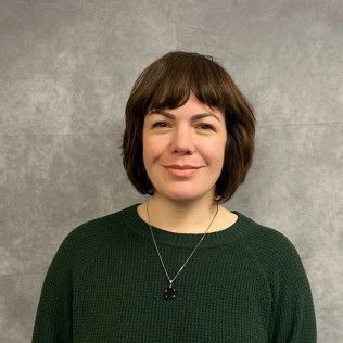 A woman wearing a green sweater and a necklace is smiling for the camera.