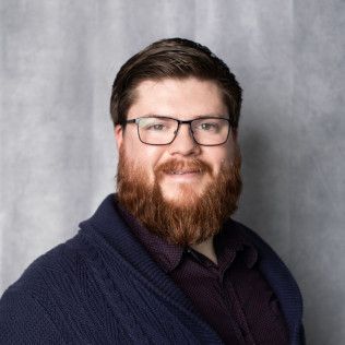 A man with a beard and glasses is wearing a blue sweater.