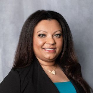 A woman wearing a black jacket and a blue shirt is smiling for the camera.