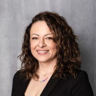 A woman with curly hair is wearing a black jacket and a necklace.