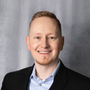 A man in a suit and blue shirt is smiling for the camera.