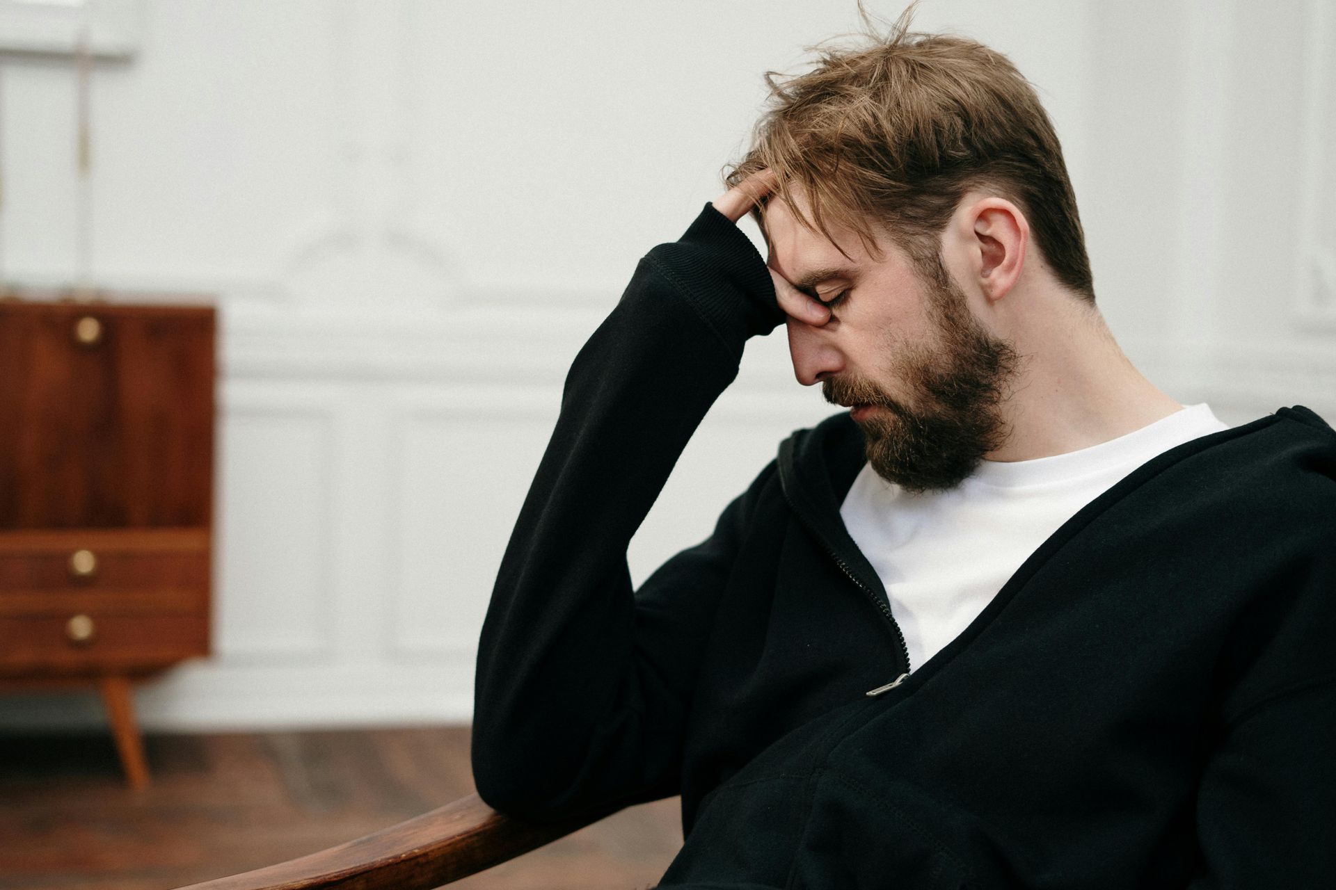 A man with a beard is sitting in a chair with his hand on his head.