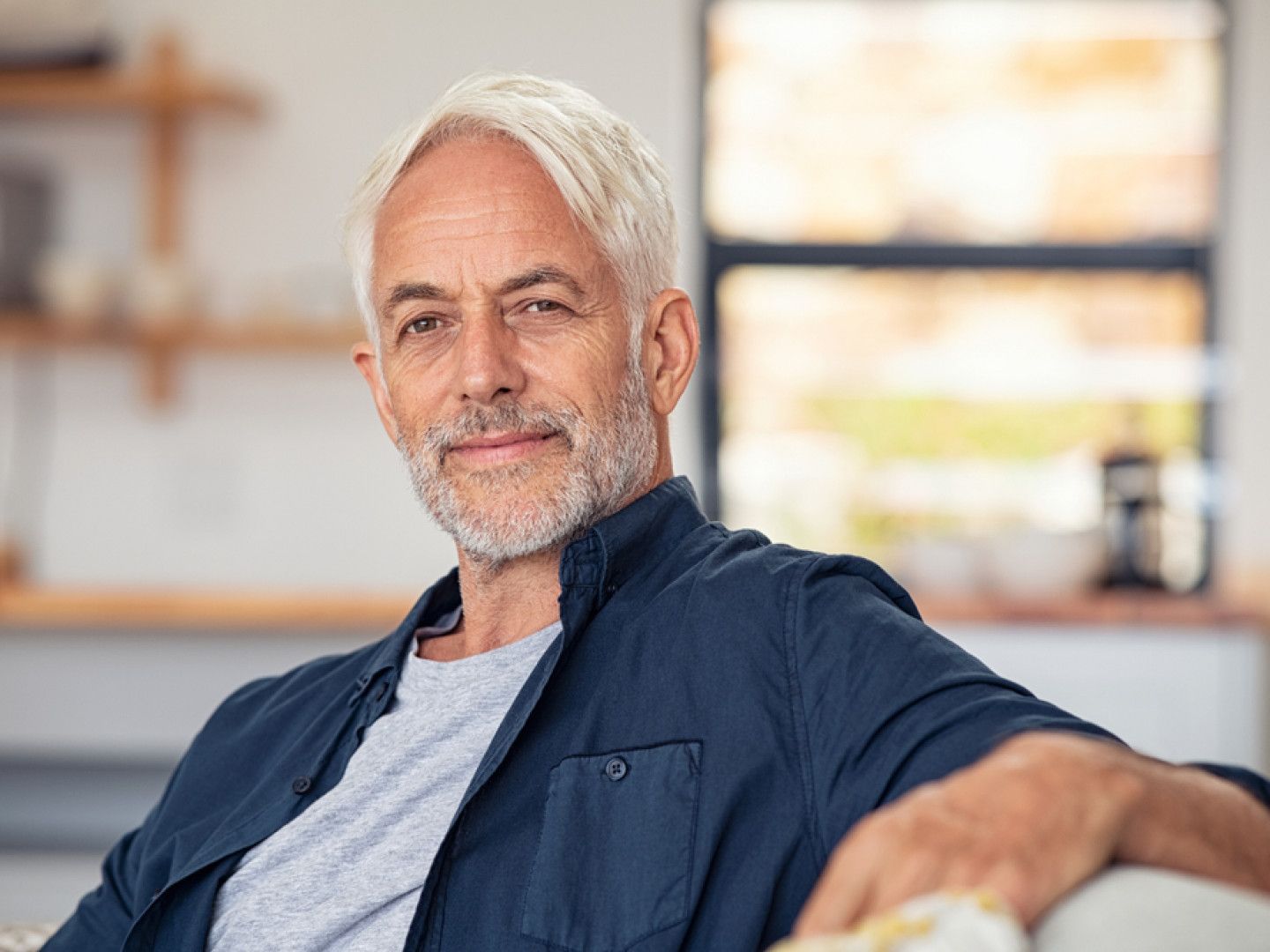 A man is sitting on a couch in a living room looking at the camera.