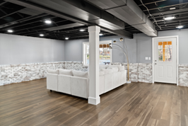 Finished basement with gray walls, white couch, stone wall, black ceiling, and wooden floor.