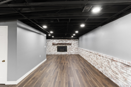 Finished basement with dark ceiling, wood floors, fireplace, and white and gray walls.