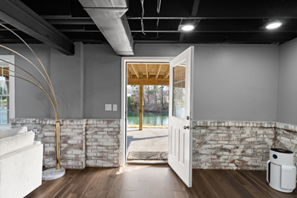 Basement interior with open door to a porch overlooking a body of water. Gray walls, black ceiling.