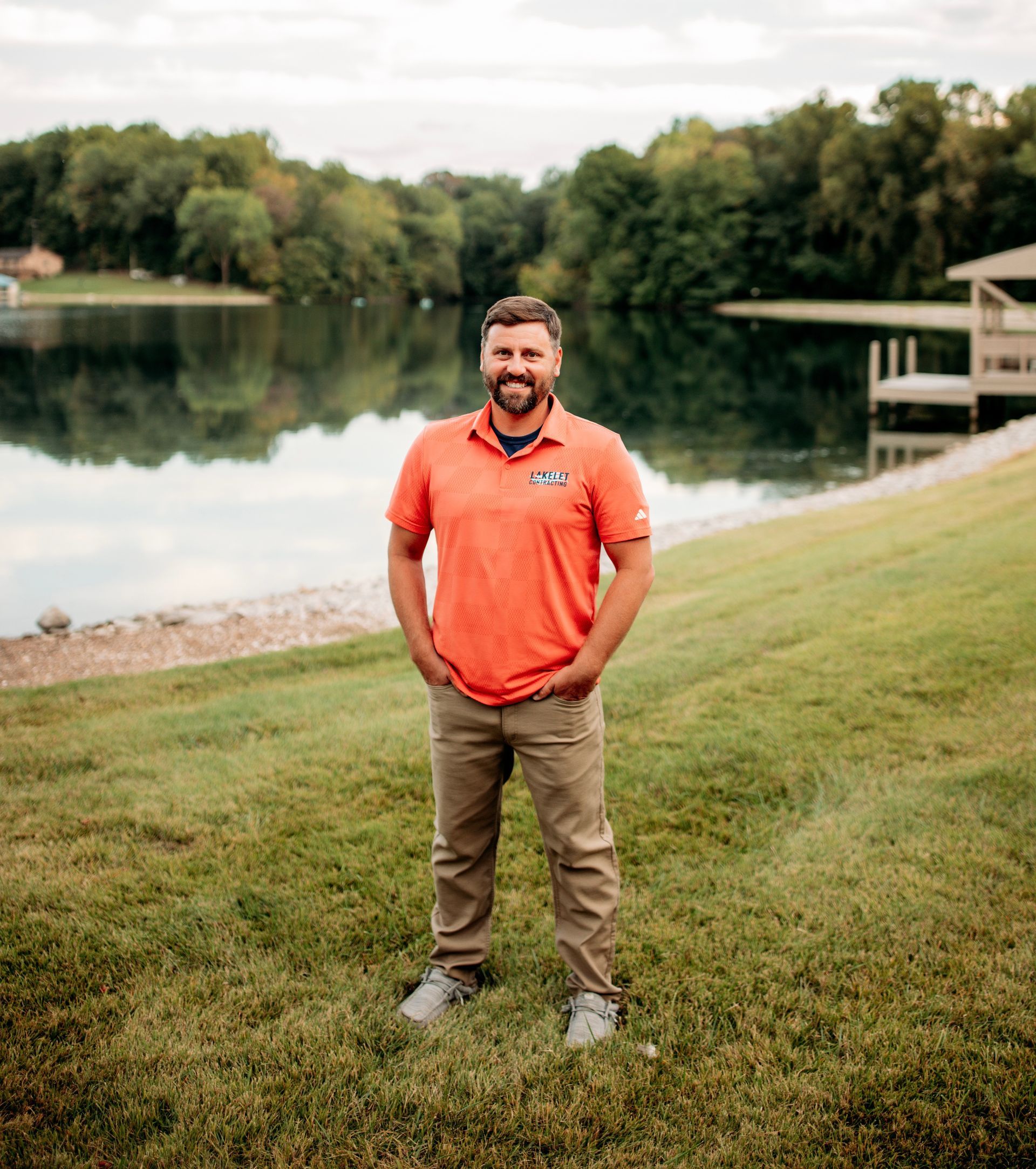 Man with crossed arms smiling in front of a weathered wooden building on a street.
