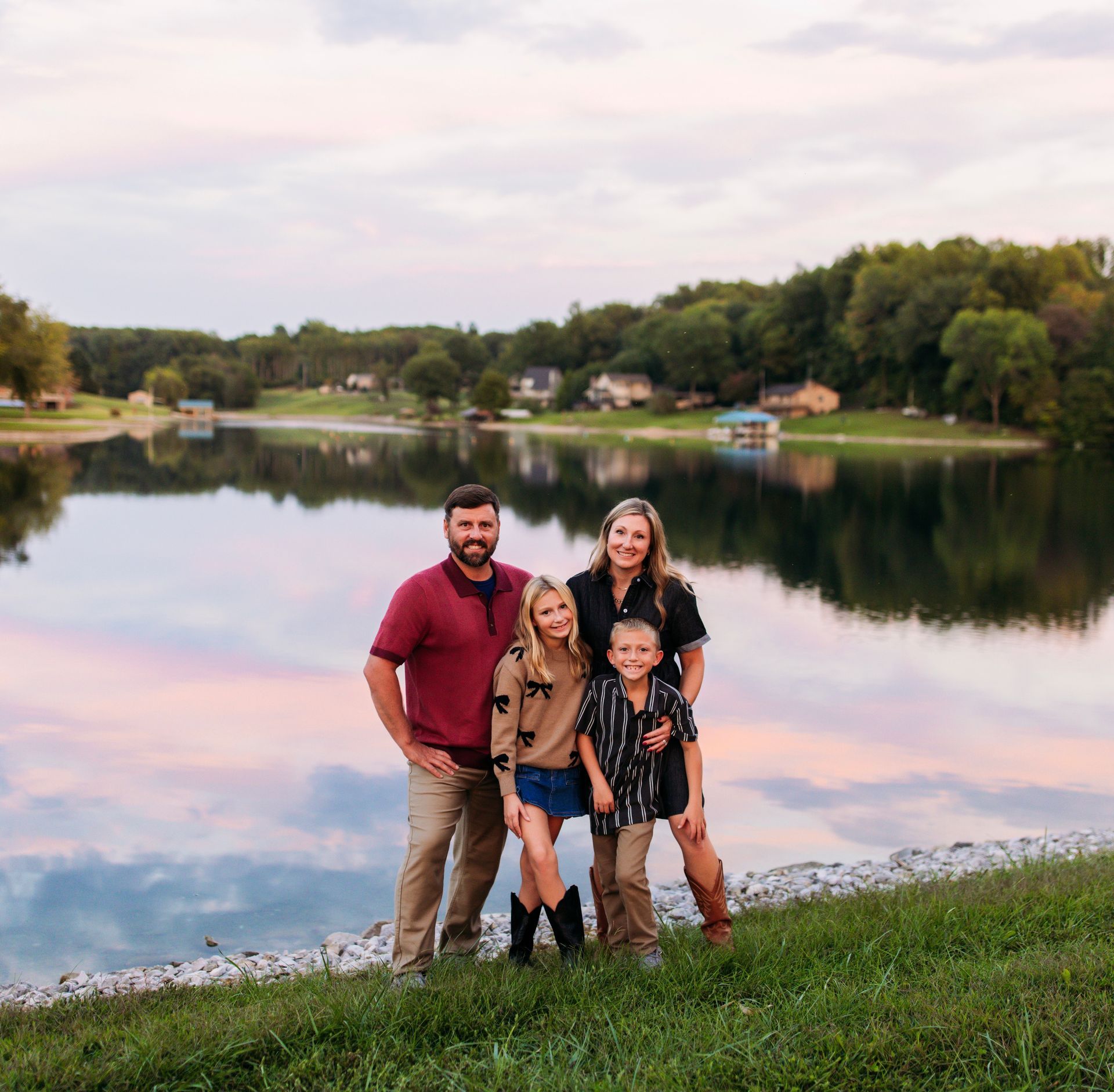 Family of four posing outdoors in front of a building. The parents embrace the children, smiling.