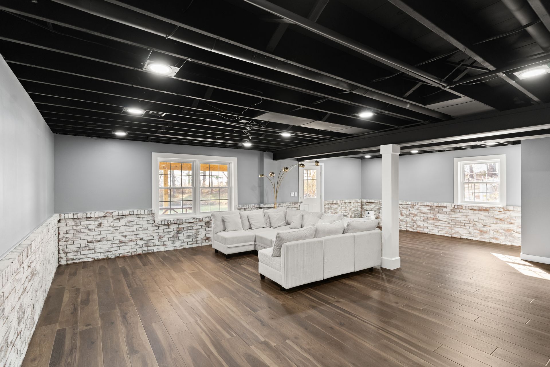 Finished basement with gray walls, black ceiling, and wood floor; white sectional.