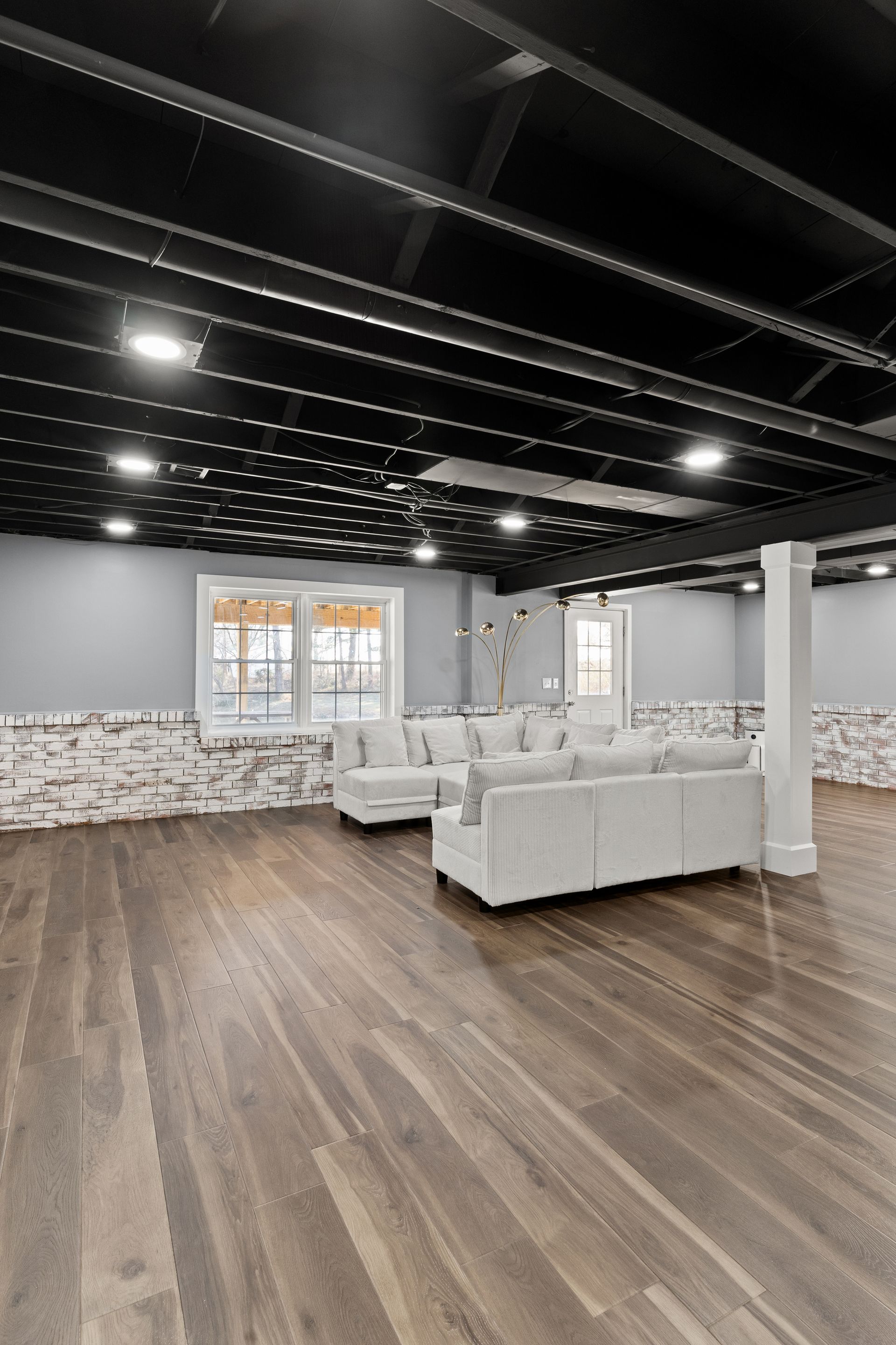 Modern living room with dark wood floors, gray walls, and a black ceiling, with a white sofa.
