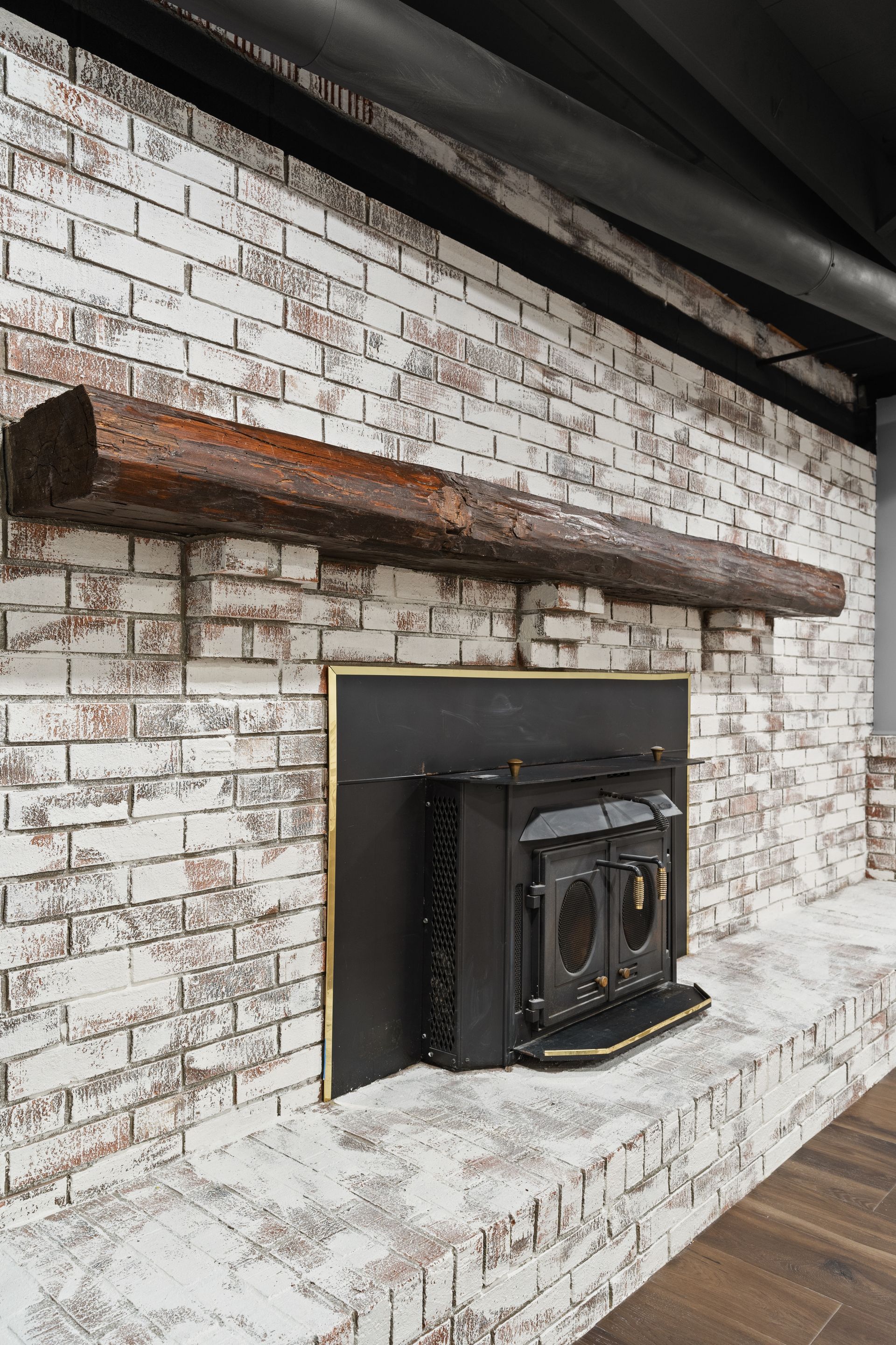 White brick fireplace with dark wood beam mantle and black stove.