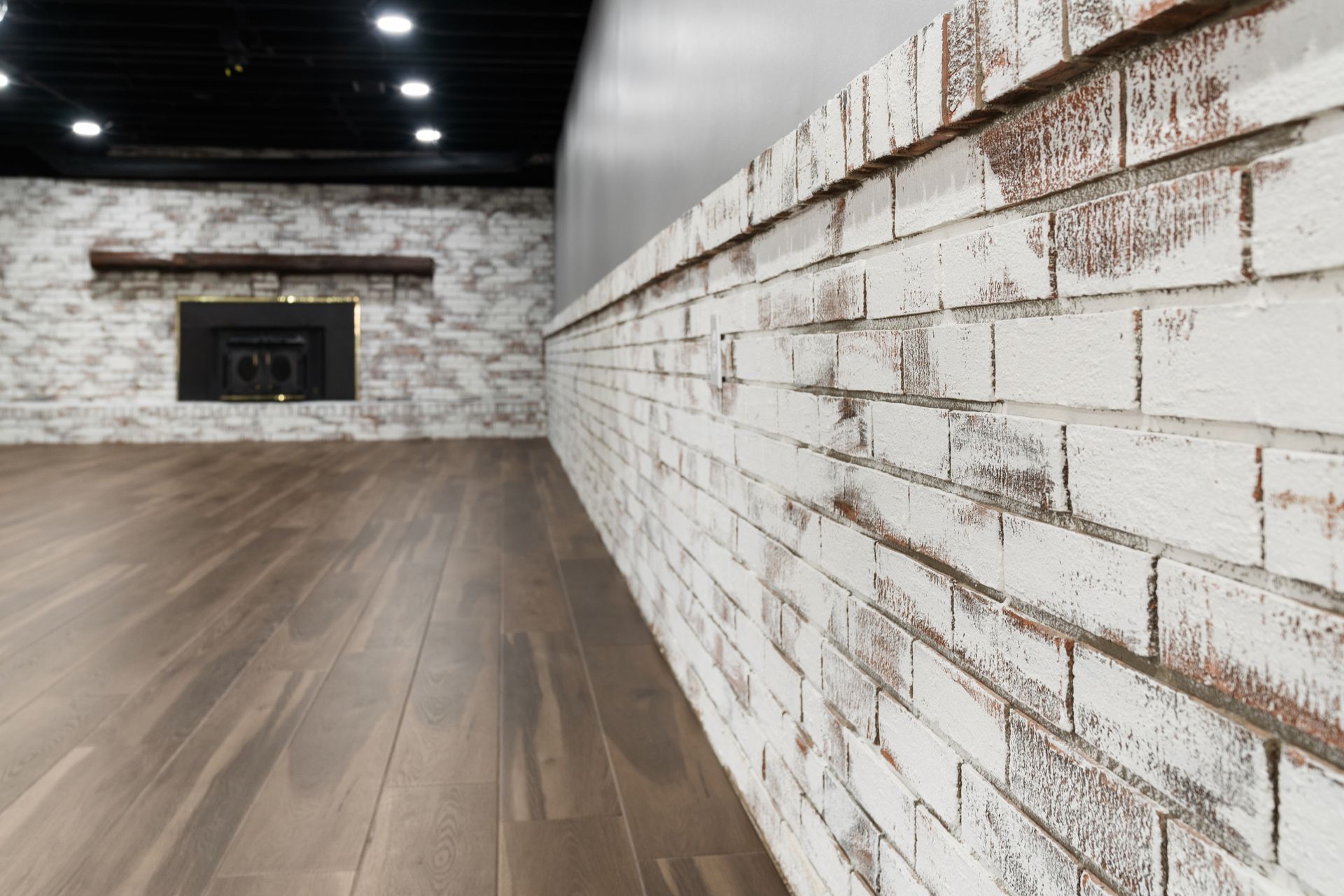 White brick wall and fireplace in a room with wood floors and a black ceiling.