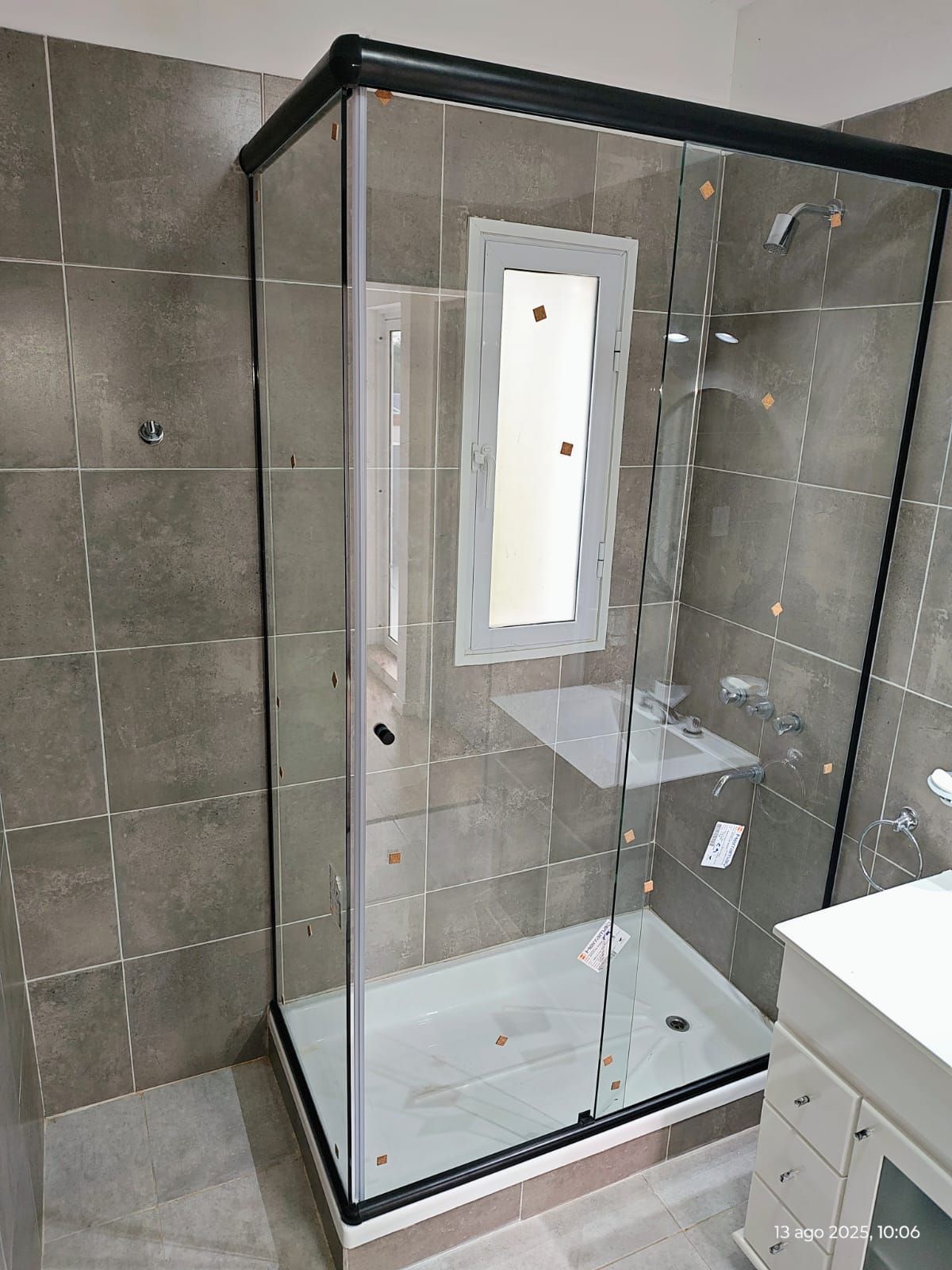 Baño moderno con ducha de cristal, lavabo y mueble de madera. Se ven un toallero y una botella de cristal decorativa.