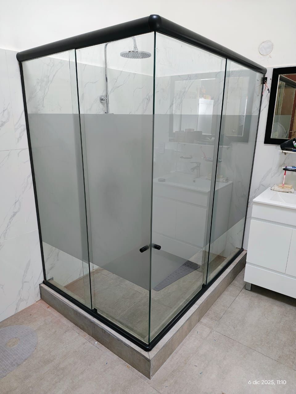 Baño con detalles en madera, ducha con mampara de cristal, suelo estampado y espejo ovalado.