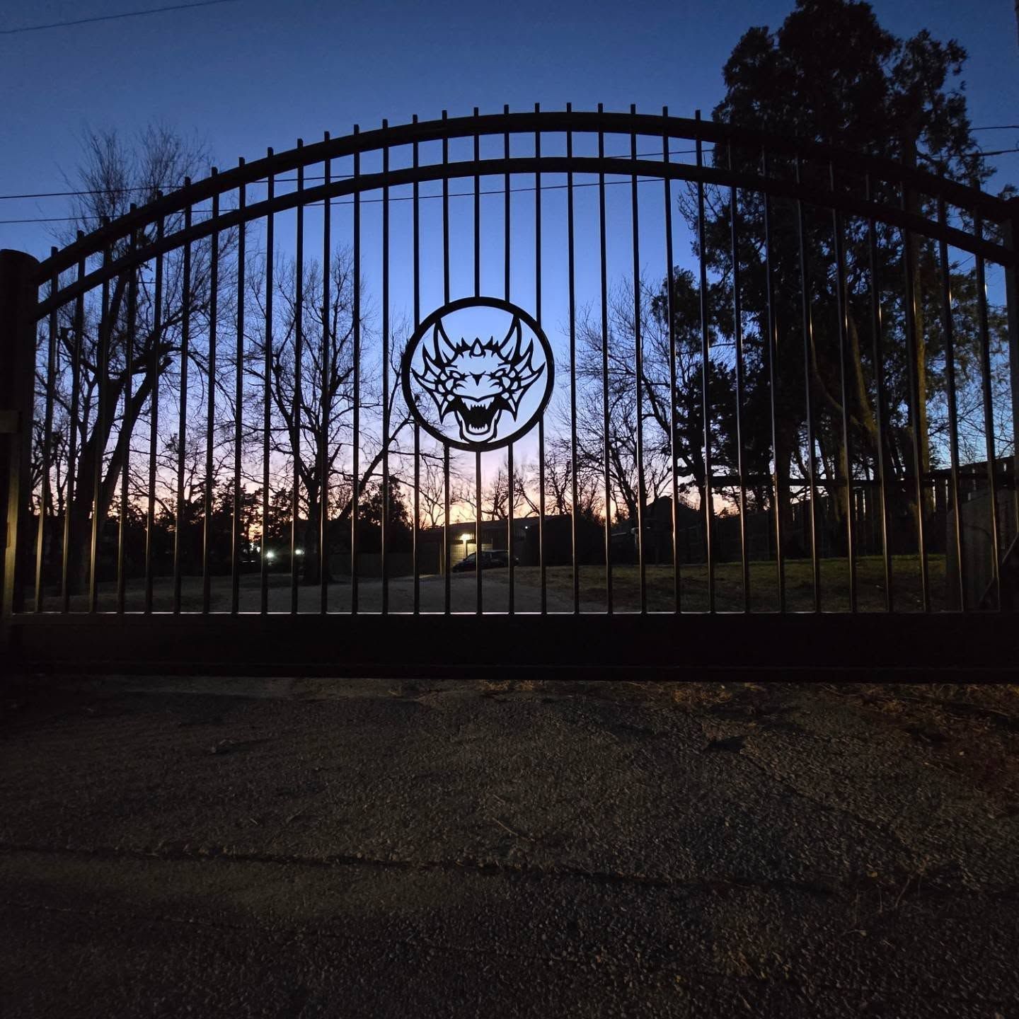 Custom ornamental iron driveway gate with decorative dragon medallion at dusk — a Legacy Fence signature installation in Oklahoma City