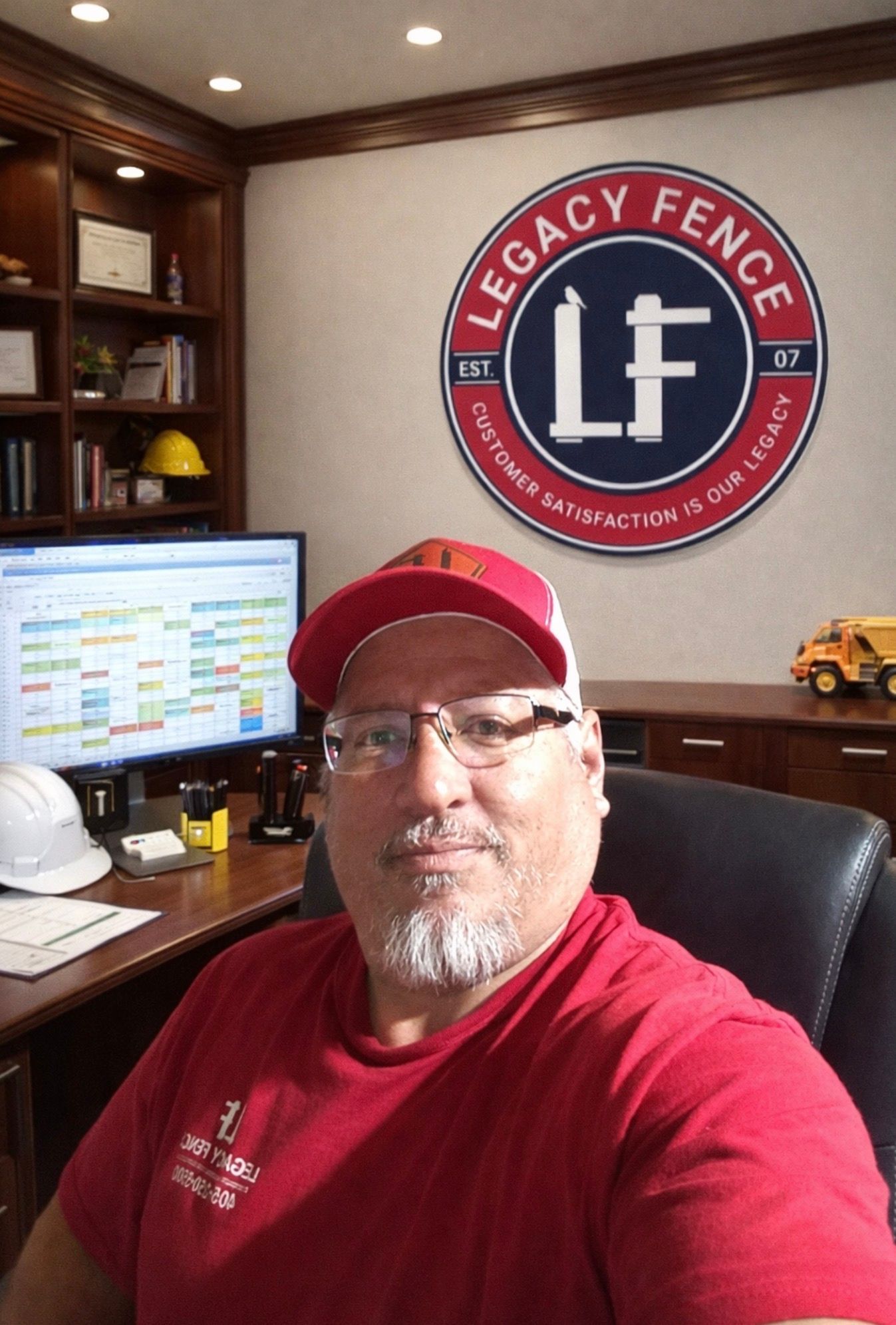 Kirby Smith, founder and owner of Legacy Fence, at his desk with the Legacy Fence logo on the wall behind him