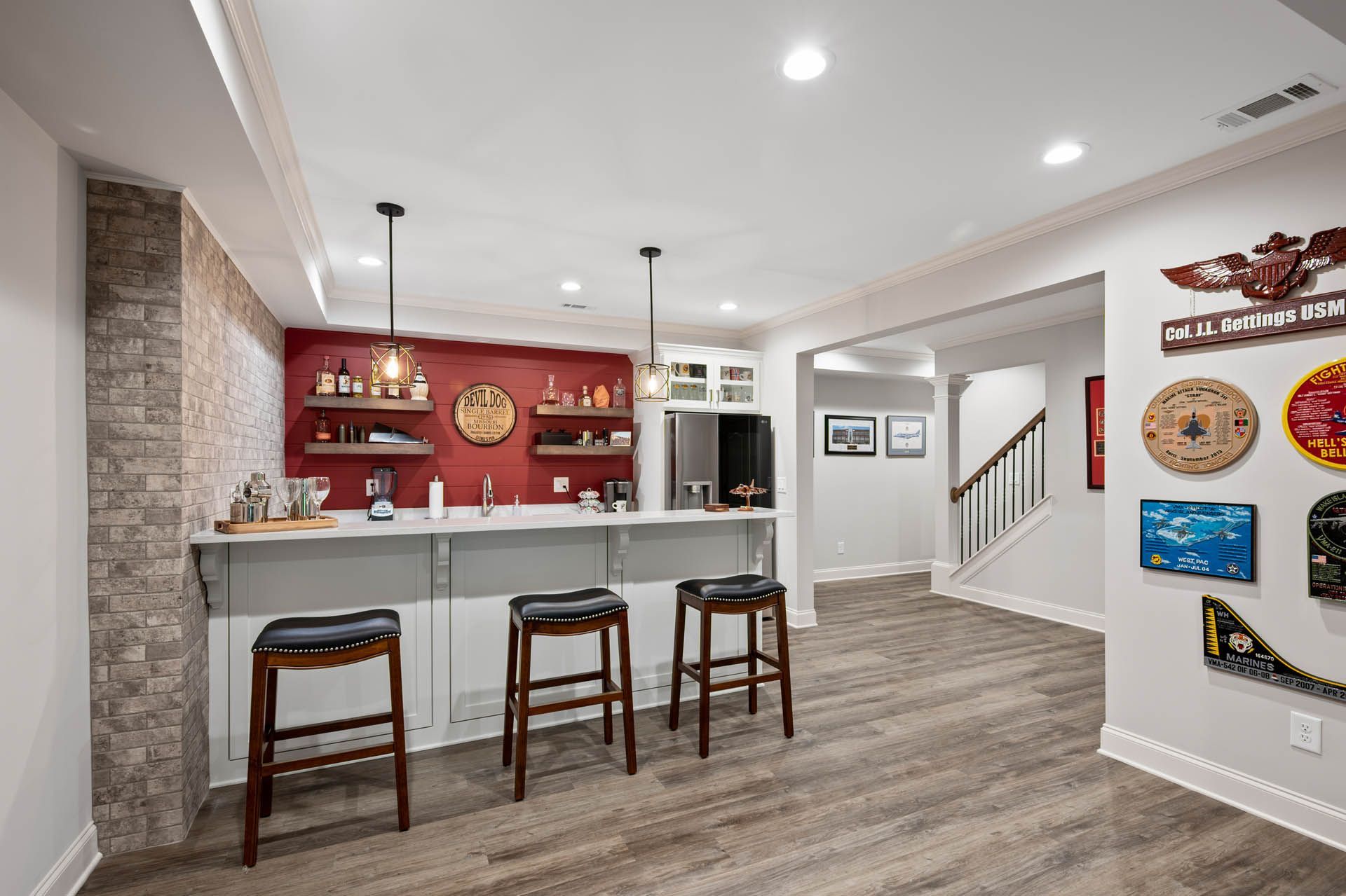 A finished basement with a bar area. There are bar stools, shelving, and decorative wall art. The flooring is a light wood grain.