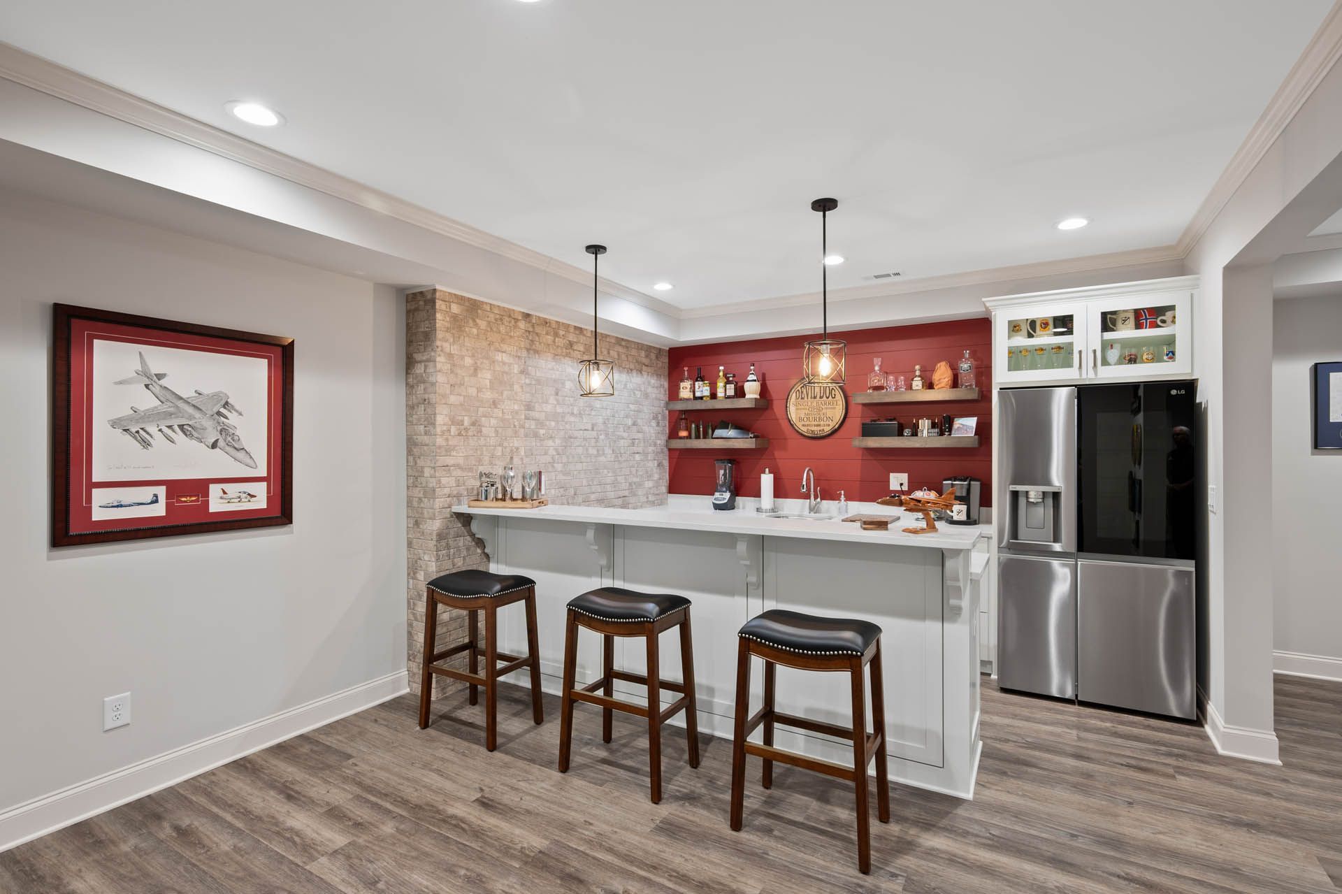 Basement bar area with a white counter, bar stools, a red wall, and a stainless steel refrigerator.