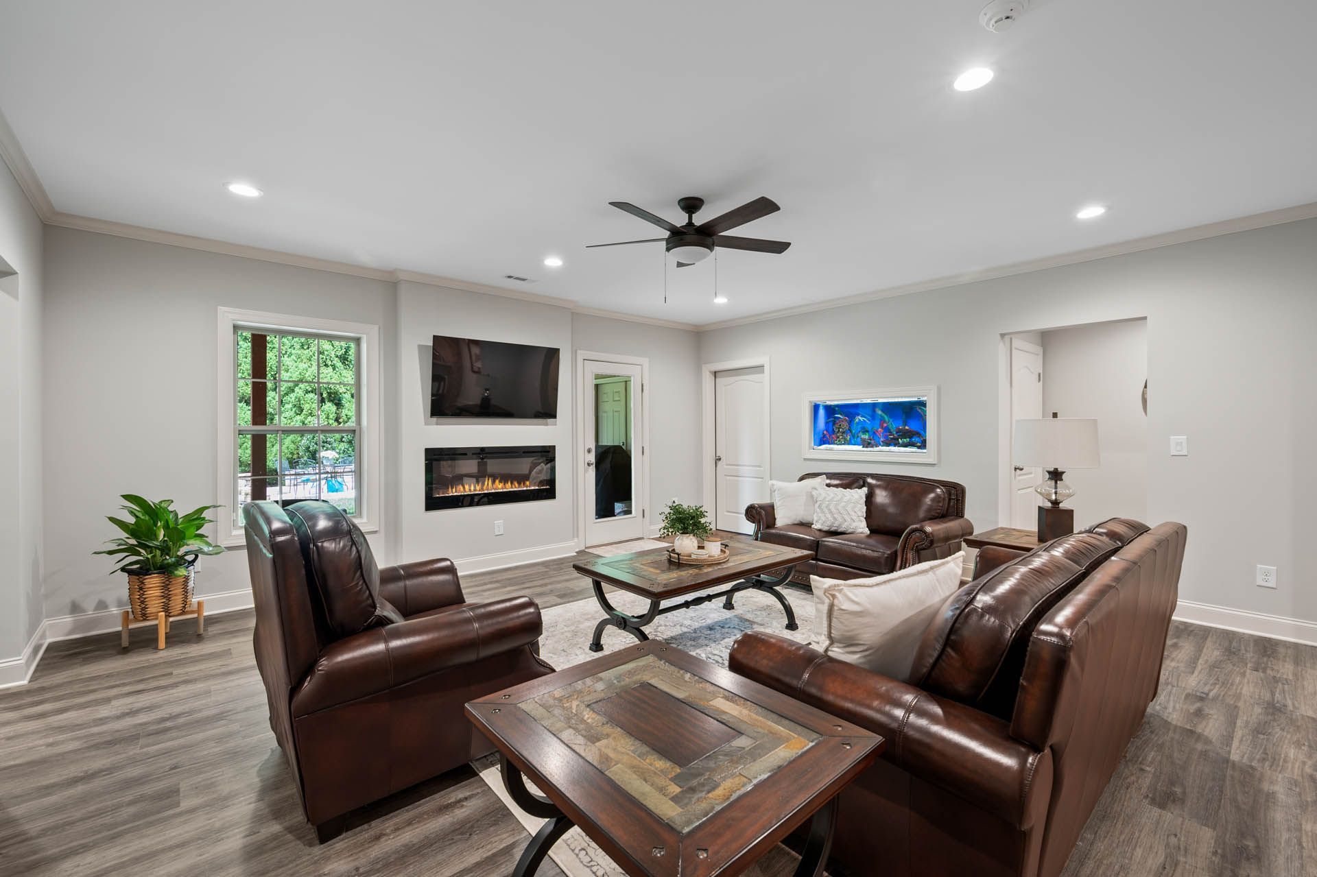 A modern living room with brown leather furniture, a fireplace, TV, and a large window.