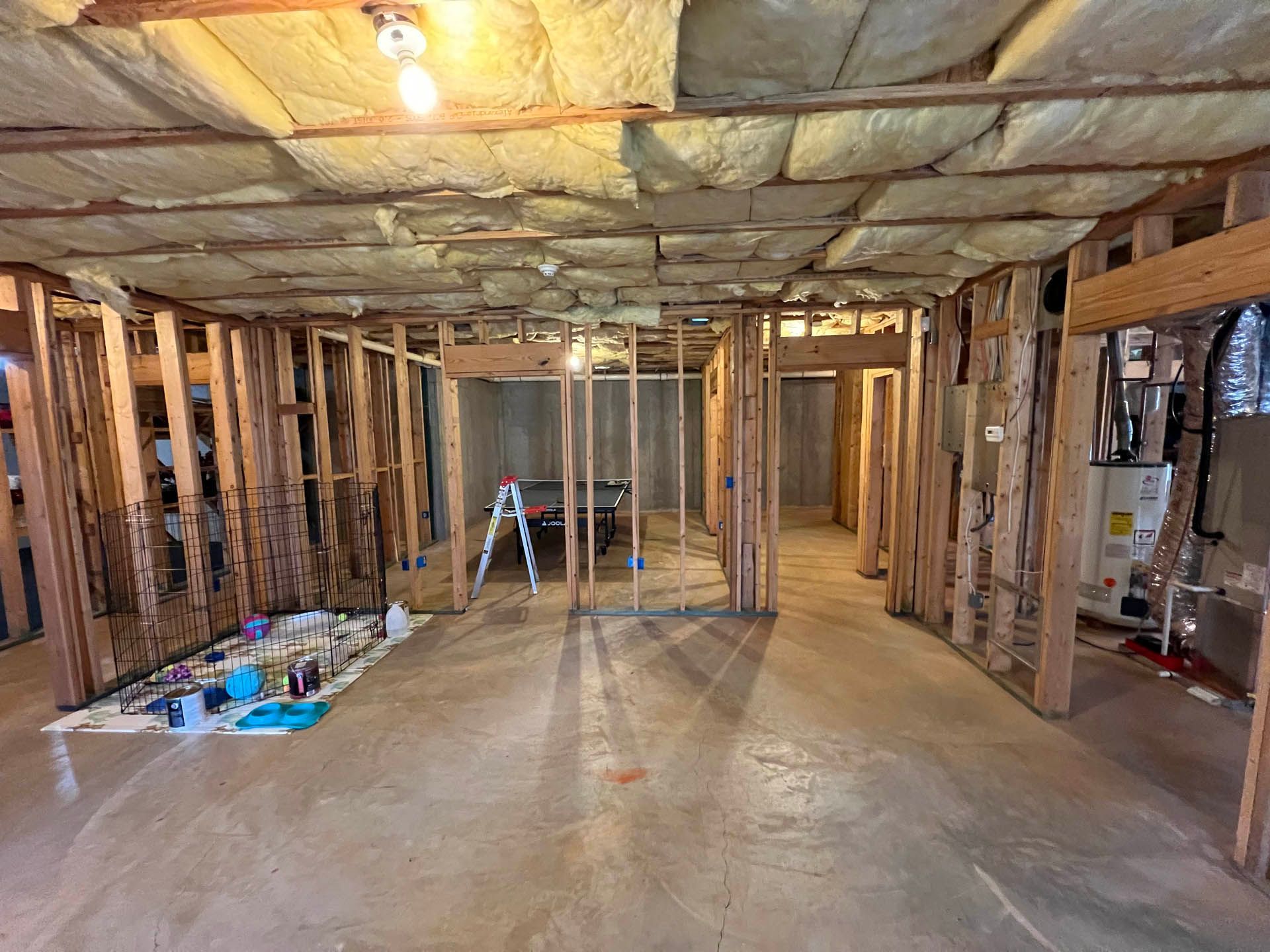 Interior of a basement under renovation; unfinished wooden frames for walls and ceiling, insulation exposed.