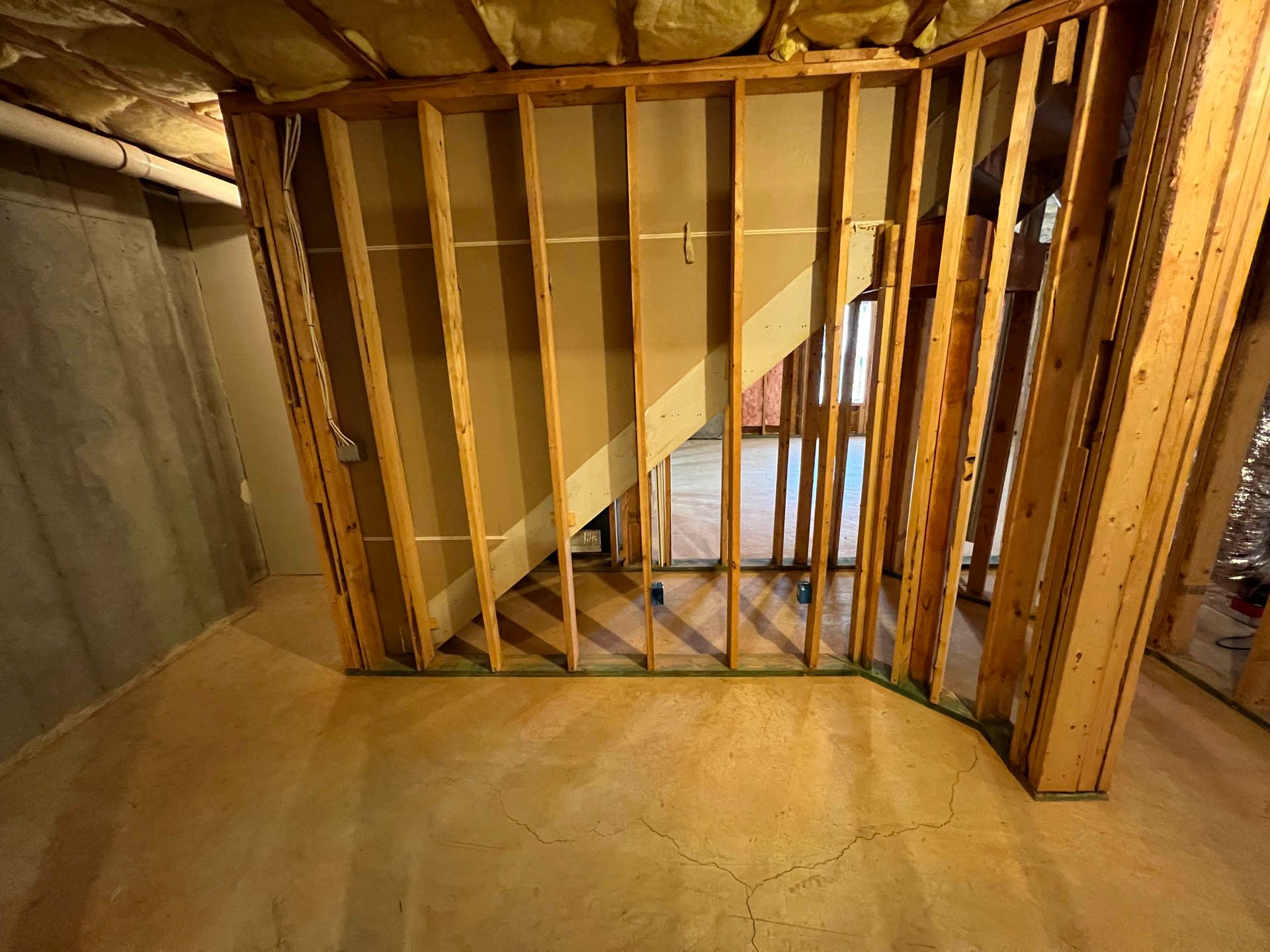 Framing for a staircase, visible in unfinished basement. Wooden studs define the stairwell and surrounding walls.