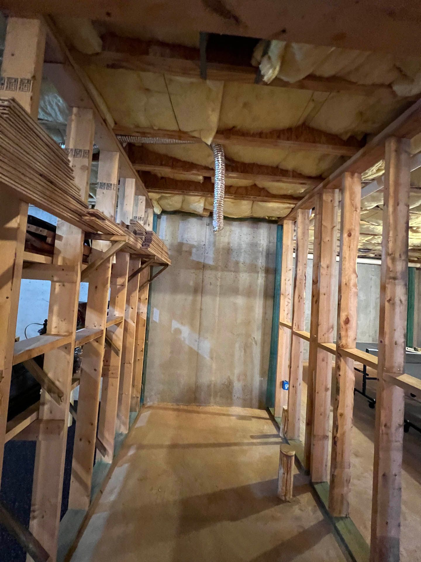Interior view of a room under construction. Wooden framing creates walls and a ceiling, with insulation visible above.