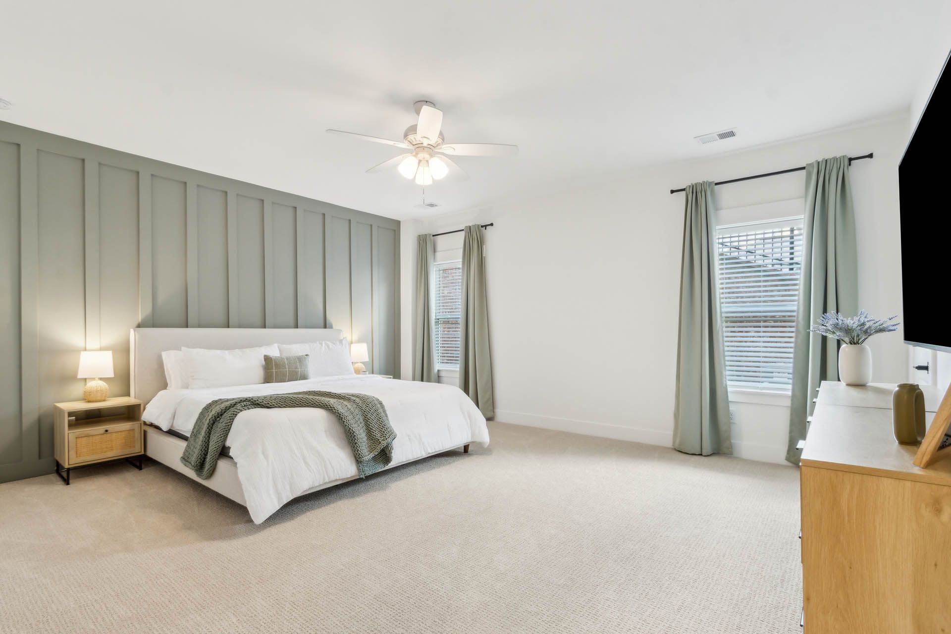 A spacious bedroom with a king-sized bed, green accent wall, and large windows with light green curtains.