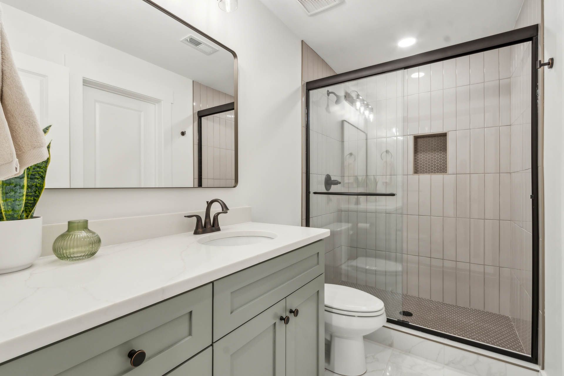 Modern bathroom with sage green vanity, white countertop, glass shower, and large mirror.
