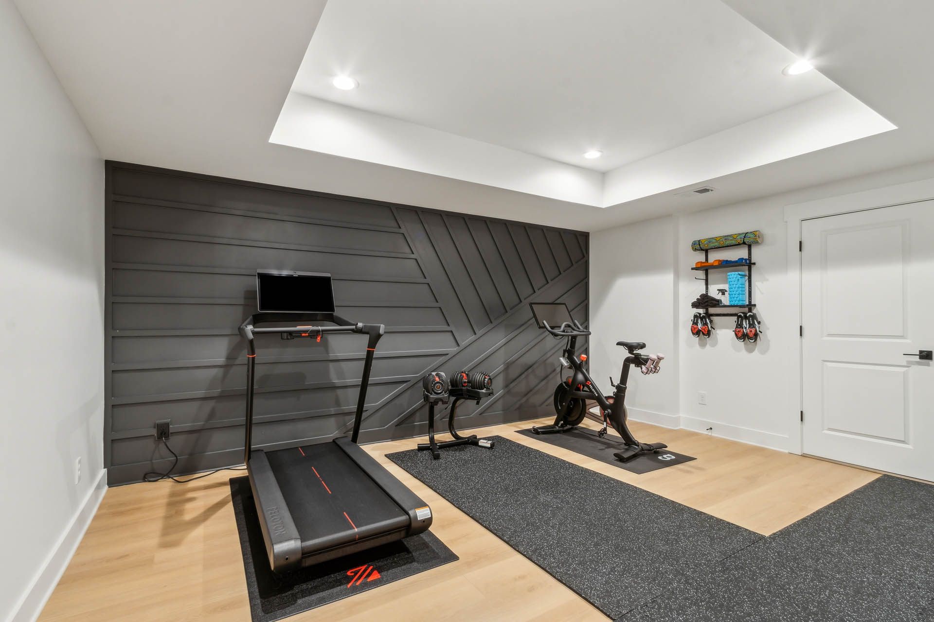 Home gym with treadmill, exercise bike, and weights on a dark accent wall and light wood floor.
